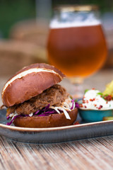Pulled pork burger on a oval plate with french fries and mayonnaise dressing and glass of beer.