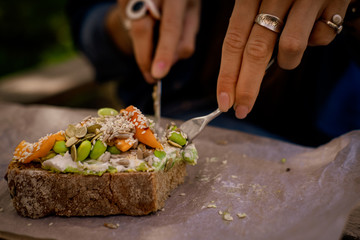 Woman hands cutting avocado toast with cream cheese, edamame, peaches. Wooden table at coffee shop.