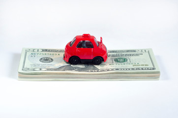 little toy red car and a stack of money banknotes american dollars on a white isolated background. vehicle loan. save up for a dream.