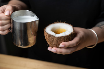 Female barista is pouring milk to make cappuccino in a coconut shell