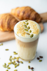 Milky latte with pumpkin seeds on froth, served on white background with french crunchy croissants