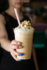 Woman is holding latte with whipped cream, toppings and straw on the outstretched hand