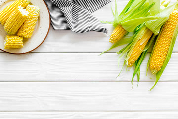 Ripe corn on cobs on plate on white wooden table background top view mock up