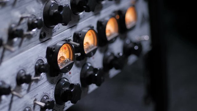 Side view of working sound compressor panel with adjusting knobs, indicator displays with needles moving during sound recording in professional music studio. Closeup work of audio compressor, blurred