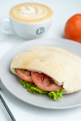 A cup of nice cappuccino and pita, stuffed with veggies and chicken breast on a white table in cafe