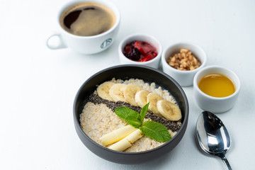 Healthy sweet breakfast with whole grain porridge, chia seeds, butter, banana and other toppings, served with a cup of black coffee on a white background