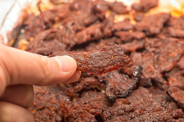 Hand holding a piece of home made beef jerky - obrazy, fototapety, plakaty