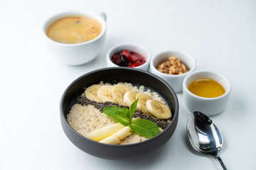 Healthy sweet breakfast with whole grain porridge, chia seeds, butter, banana and other toppings, served with a cup of black coffee on a white background