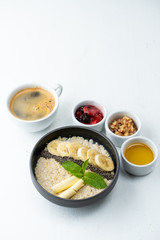 Healthy sweet breakfast with whole grain porridge, chia seeds, butter, banana and other toppings, served with a cup of black coffee on a white background