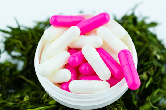 White Medical Medicine Box With Colorful Pills On The Background Of A Pile Of Medical Cannabis. The Concept Of Replacing Opioids With Cannabis