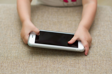 a small child took a white smartphone from a sofa and holds it in his hands