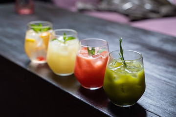 Row of multicolored herbal and fruit tea with lemon, strawberry, matcha and berries, placed on a blurred cafe background