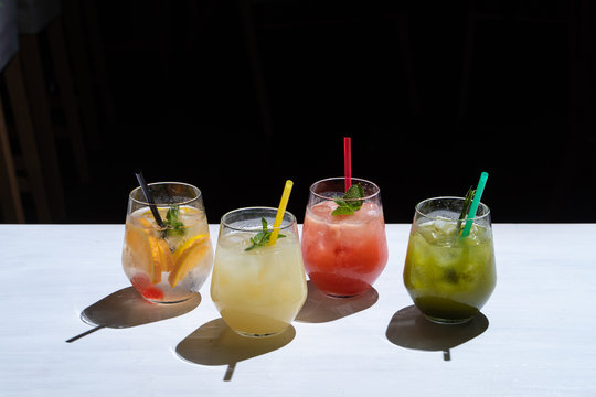 Side view of various of refreshing summer lemonades: classic lemon soda, strawberry lemonade, ginger spicy lemonade and estragon soda served on a white background