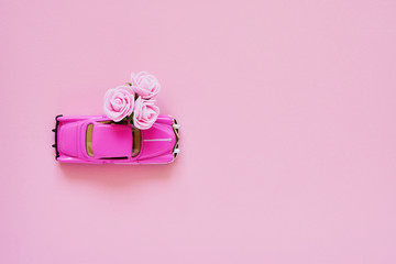 Obraz na płótnie Canvas Riga, Latvia - July 28, 2019. Pink retro toy car delivering pink flowers bouquet on pink background. Top view, copy space. Flowers delivery.
