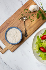 Homemade Buttermilk Ranch Dressing in Blue Bowl on White Countertop; Prepared Salad in Background
