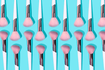 Pattern made of make up white brush on turquoise background. Minimal beauty concept.
