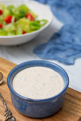 Homemade Buttermilk Ranch Dressing in Blue Bowl on White Countertop; Prepared Salad in Background