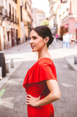 Portrait of young woman with topknot hairstyle smiling and wearing red ruffles dress walking on the...