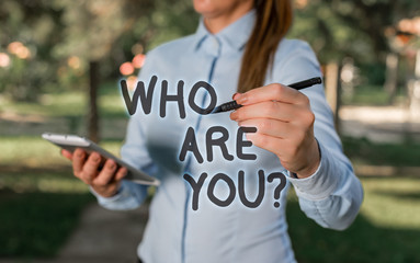Conceptual hand writing showing Who Are You question. Concept meaning asking about demonstrating identity or demonstratingal information Woman in a blue shirt pointing with her finger into empty space