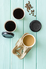 Caution: contents hot. Beans, black coffee and coffee with milk to-go on mint green wooden background top view
