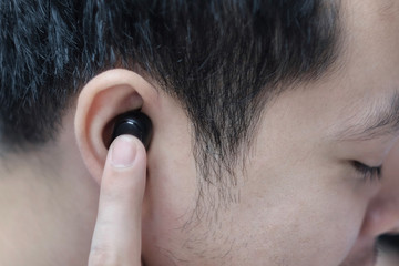 A young man commands a smart phone via black wireless bluetooth headphones.