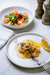 Tiger prawns on the grill with sause and greens on white concrete table