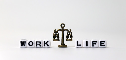 A miniature scale between WORK word and LIFE word on white cubes.