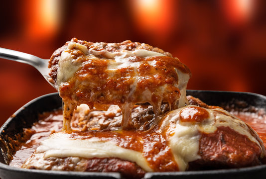 Parmegiana Steak isolated also known as Filet Parmegiana in a black iron pan on a wooden fire background out of focus, cheese and tomato sauce. Soft light, angle view