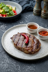 juicy Ribeye steak on white plate on dark grey concrete table