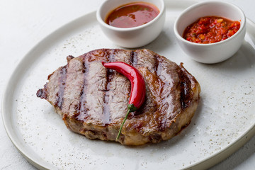 juicy Ribeye steak on white plate on white concrete table