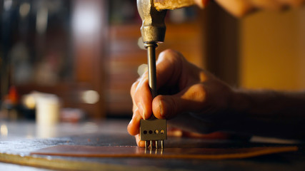 Tanner makes hole in workpiece. Male hands close up holding tool. Leathercraft concept..