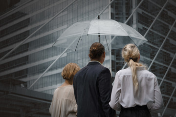 caucasian business people walking outdoors on street with umbrella when raining