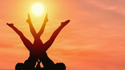 Fototapeta na wymiar silhouette of two caucasian female posing yoga style with background of sunrising sky