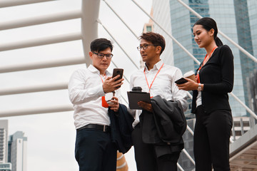 asian business people with tablet and smartphone on hands standing and having business conversation outdoors urban