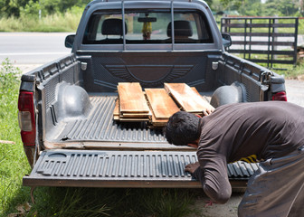 Carpenter counting pile of lumber woods and palnks on pick up truck. Woodworking concept.