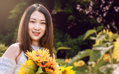 Naklejka premium A young oriental girl with long hair and white dress in a field of sunflowers