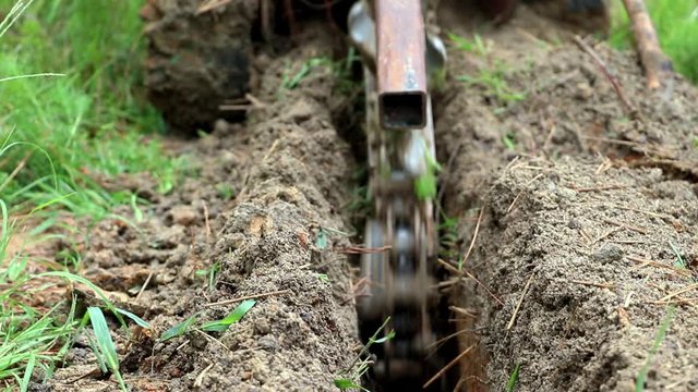 Slow motion, close up view of machine digging a trench for backyard irrigation system. Landscape design and trenching for pipe, conduit or utilities. Large chain spinning to dig a channel in dirt.