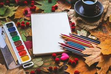 notebook and pencils. a cup of coffee. stationery on a background of autumn leaves.