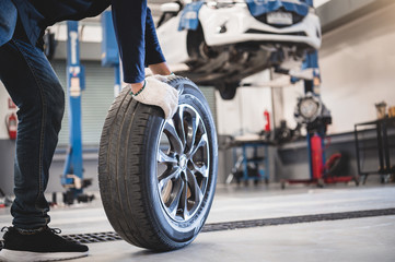 Male mechanic hold and rolling tire at repairing service garage background. Technician man...