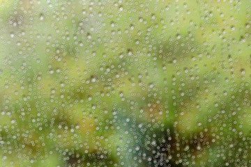 Blurred water drop on glass with ring bokeh and green nature background.