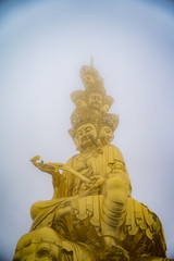 Fototapeta na wymiar Golden Puxian statue of Mt. Emei on a foggy day