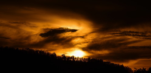 Picture of a sun setting behind a dense forest area followed by mountains	