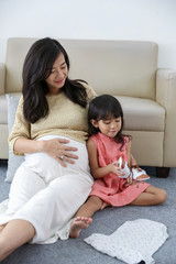 asian little girl holding baby shoes to show her mother