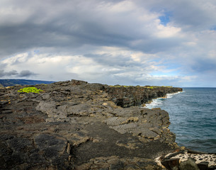 Fototapeta na wymiar Old cracked dark lava rock in the foreground leading to tall cliffs over the ocean near the Holei Sea Arch on the big island of Hawaii