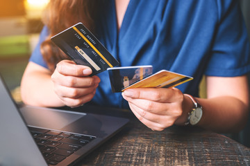 Closeup image of a woman holding and choosing credit cards while using laptop computer