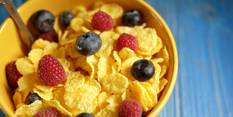 Cornflakes with berries raspberries and blueberries on blue wooden background.