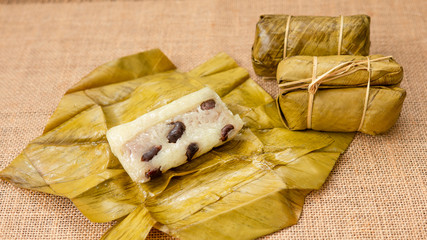 Thai dessert sticky rice or Khao Tom Mad, Wrapped the banana in sweet sticky rice on a banana leaf with sackcloth background.