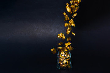 Falling gold nuggets or gold ore and glass jar in dark room