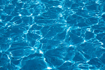 Blue and bright ripple water surface in swimming pool with sun reflection.