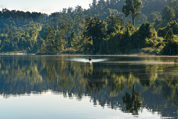 Fototapeta na wymiar Unknown canoeist paddling across the serene lake in New Zealand